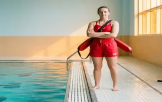 Zertifizierter Rettungsschwimmer in Uniform am Rand eines Hallenbades mit türkisfarbenem Wasser und Rettungsausrüstung.