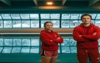 Zertifizierter Bademeister in roter Uniform steht an einem Hallenbad mit türkisfarbenem Wasser und vereisten Dachfenstern im Winter.