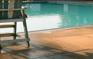 Leerer Rettungsschwimmer-Stuhl mit hängendem Rettungsring an einem sonnigen öffentlichen Schwimmbad mit türkisem Wasser.