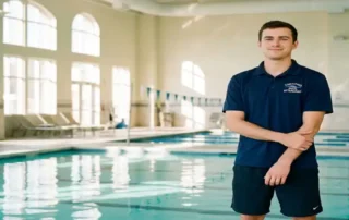 Zertifizierter Bademeister in Marineuniform steht entspannt am Rand eines Hallenbades mit türkisfarbenem Wasser und Morgenlicht.